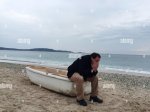 sad-man-sitting-on-boat-at-beach-against-sky-WGDNT4.jpg